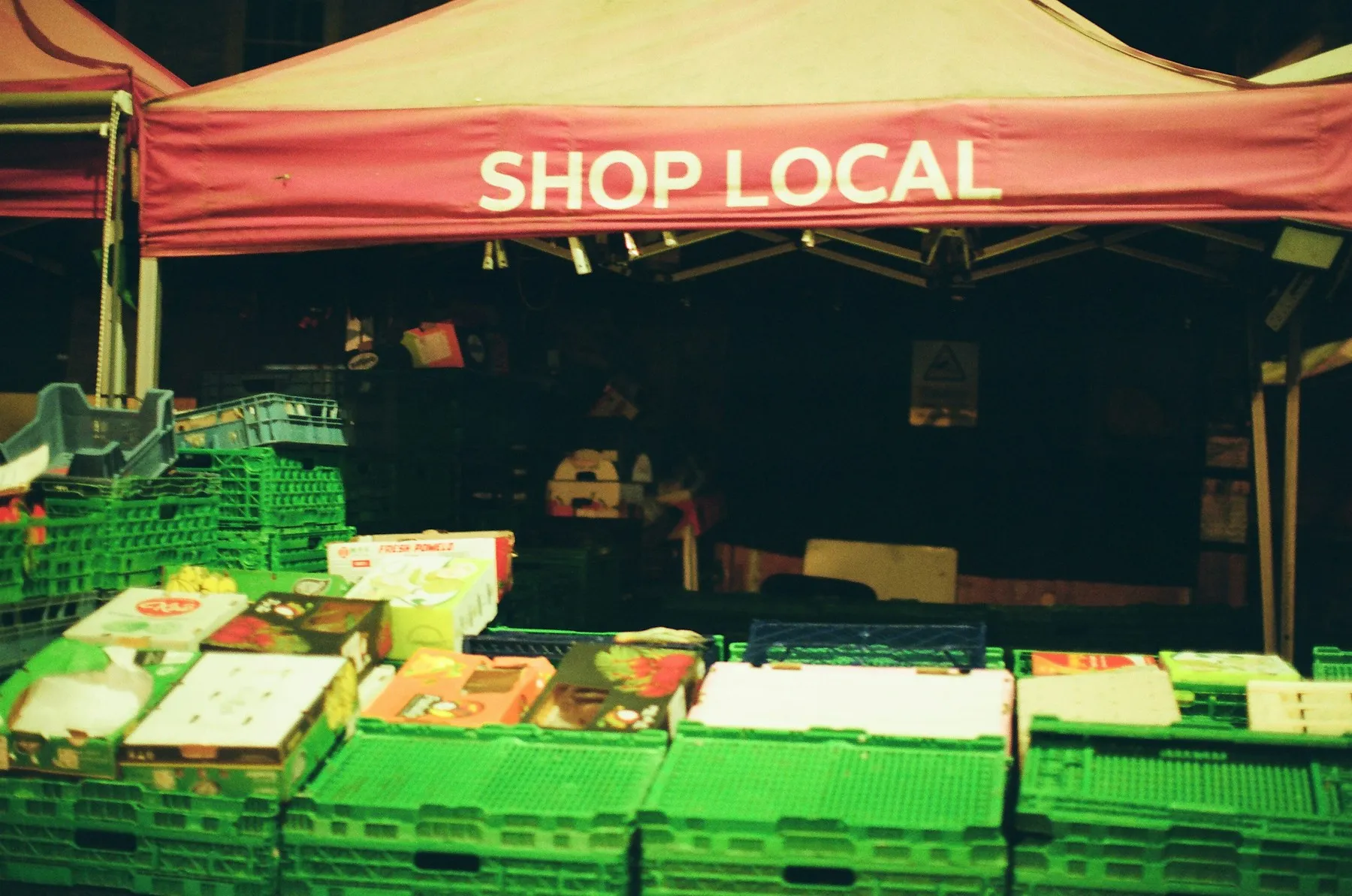 A farmers market stall stocked with fresh produce under a 'shop local' banner