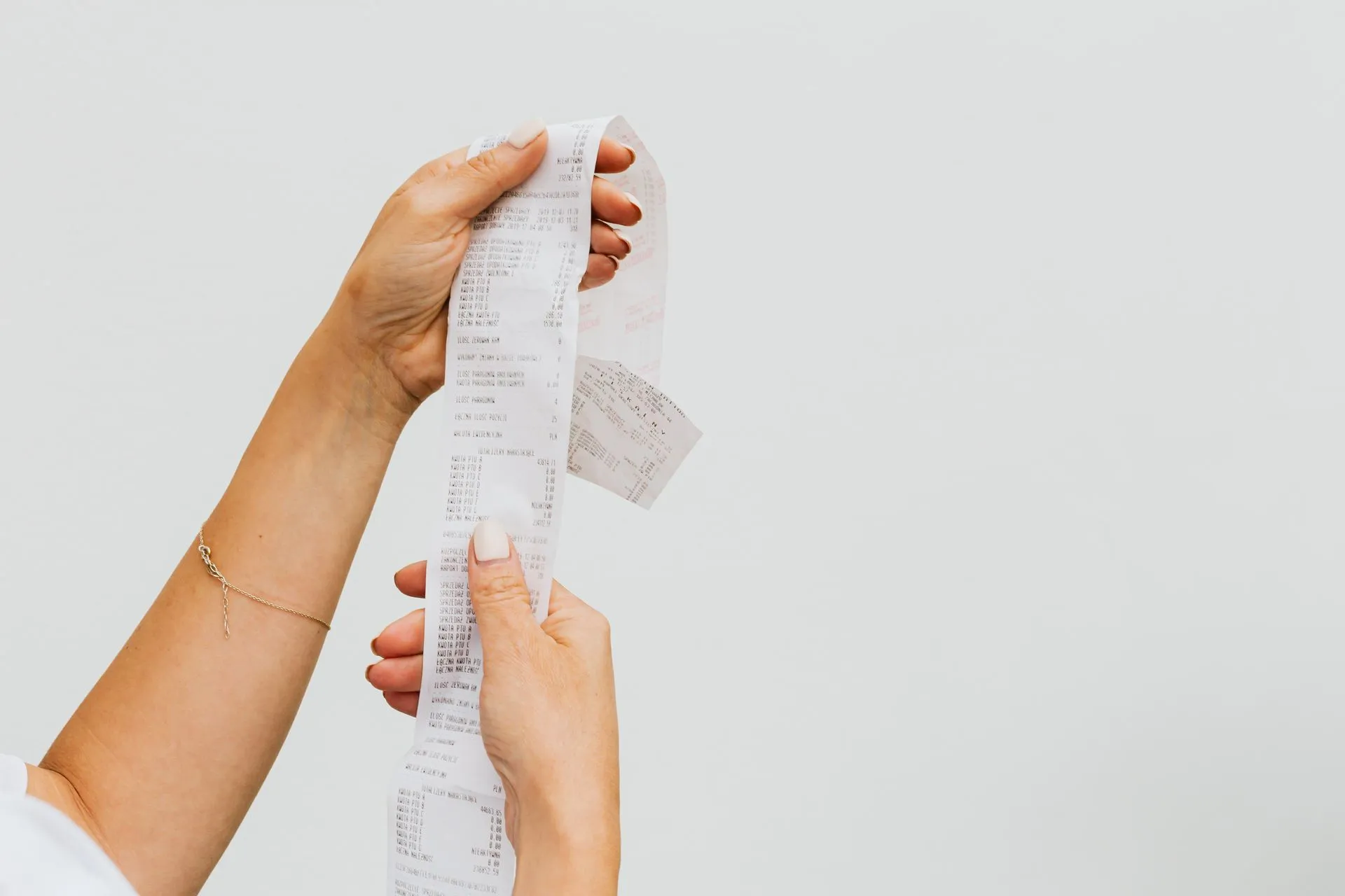 Hands holding a long printed shopping receipt against a plain white background