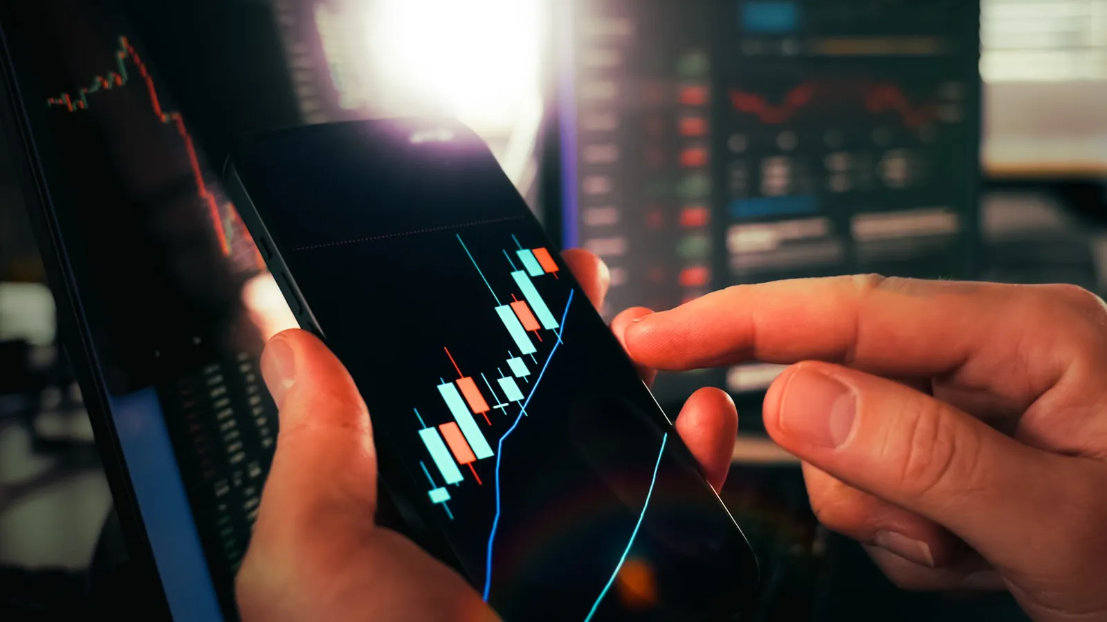 Hands holding a smartphone displaying a red-and-white stock candlestick chart